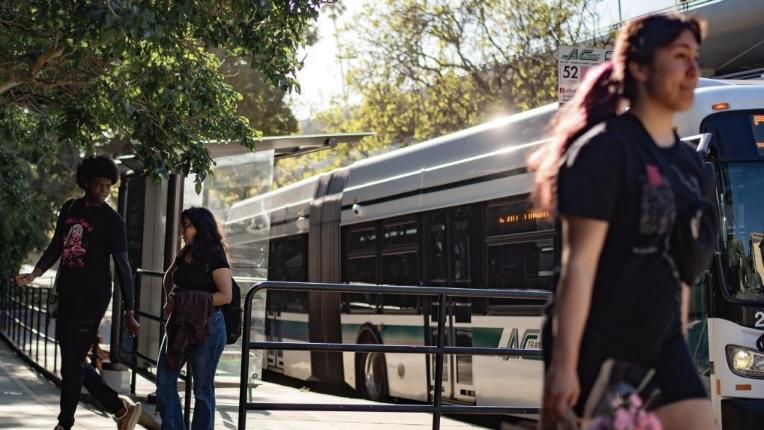 Pedestrians walking near an AC Transit Bus with Bus at the stop